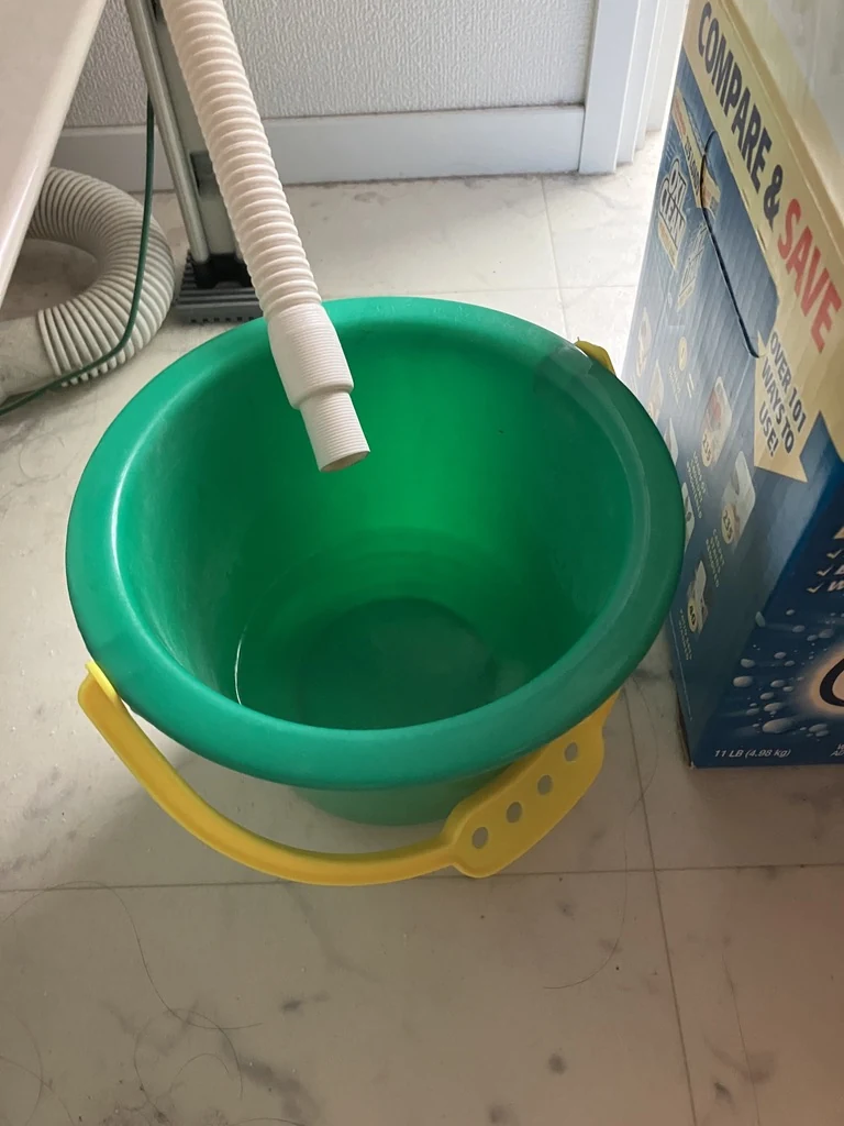 わが家の乾燥機の排水ホースと、水を受ける緑色のバケツ